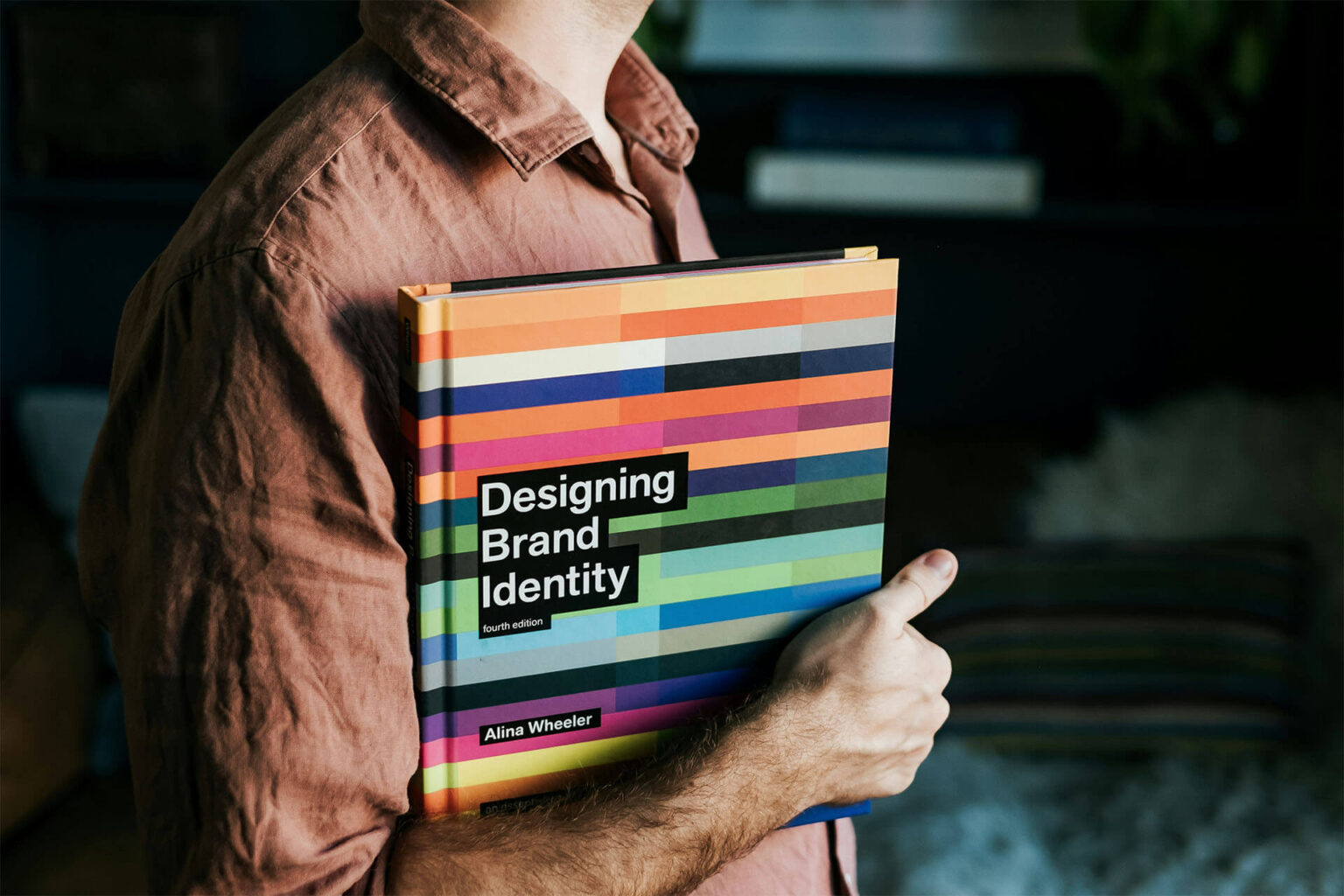 Person hält das Buch „Designing Brand Identity“ unter dem Arm